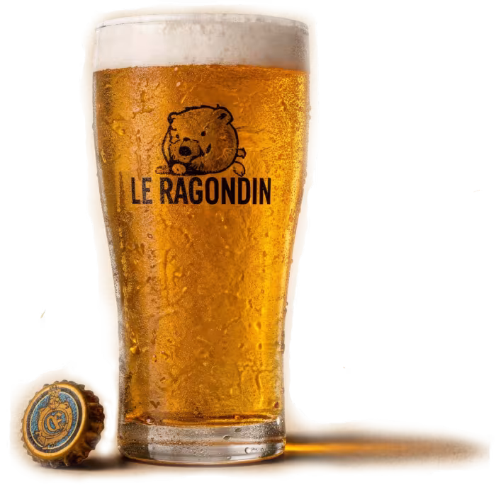 Pint glass of cold German lager with the Le Ragondin logo, beside a bottle cap